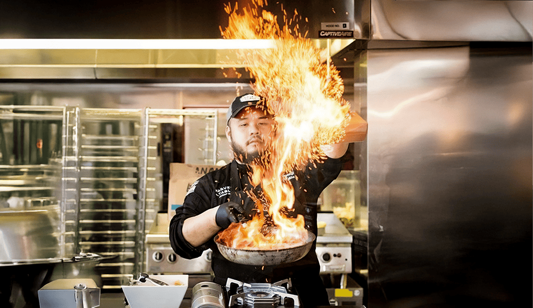 Chef cooking seafood with large flame in frying pan over heat