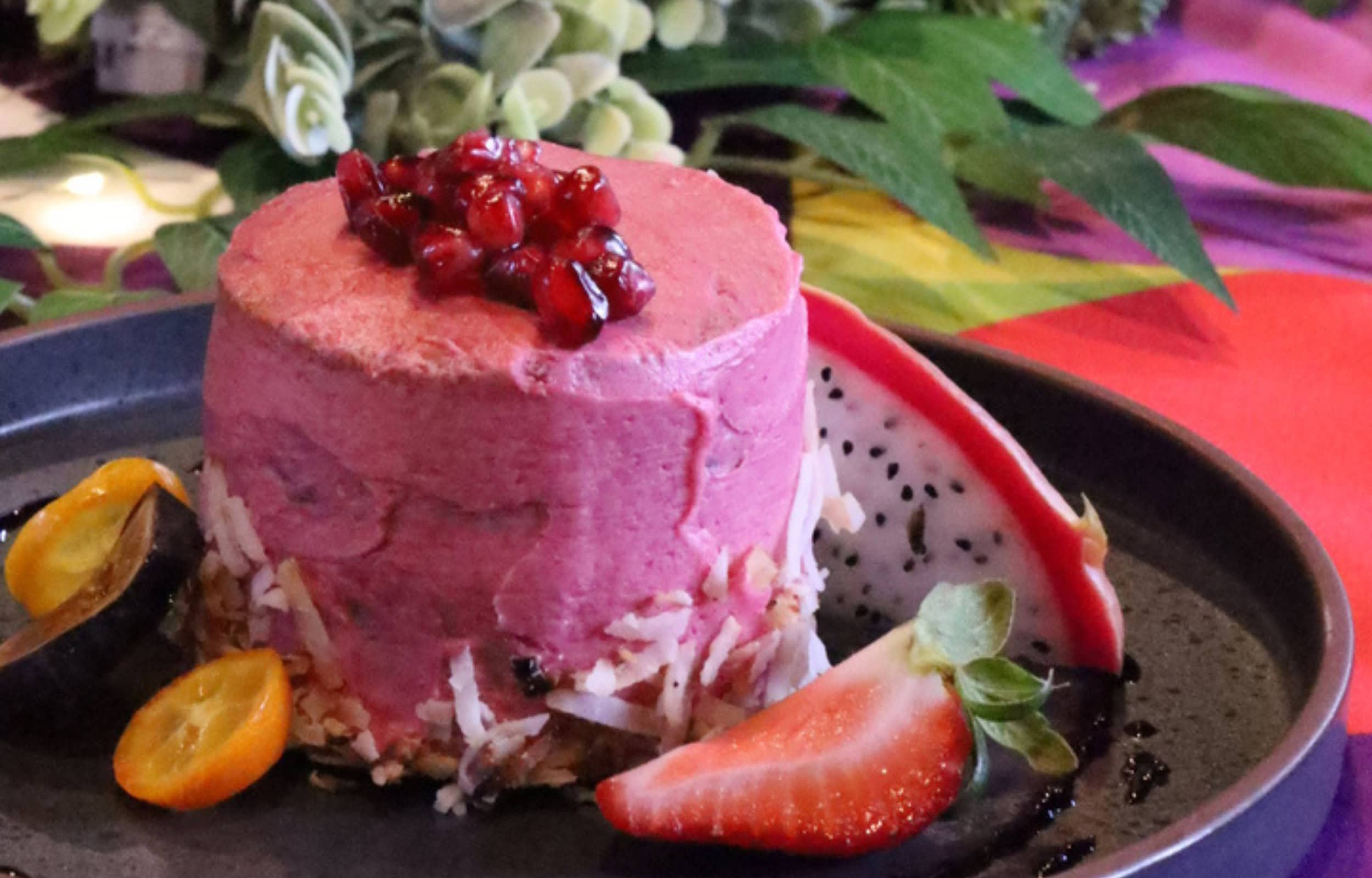 close up shot of pink dessert with strawberries, dragon fruit and pomegranate seeds